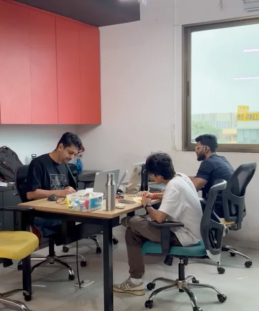 Three designers working side by side at a shared desk by the window