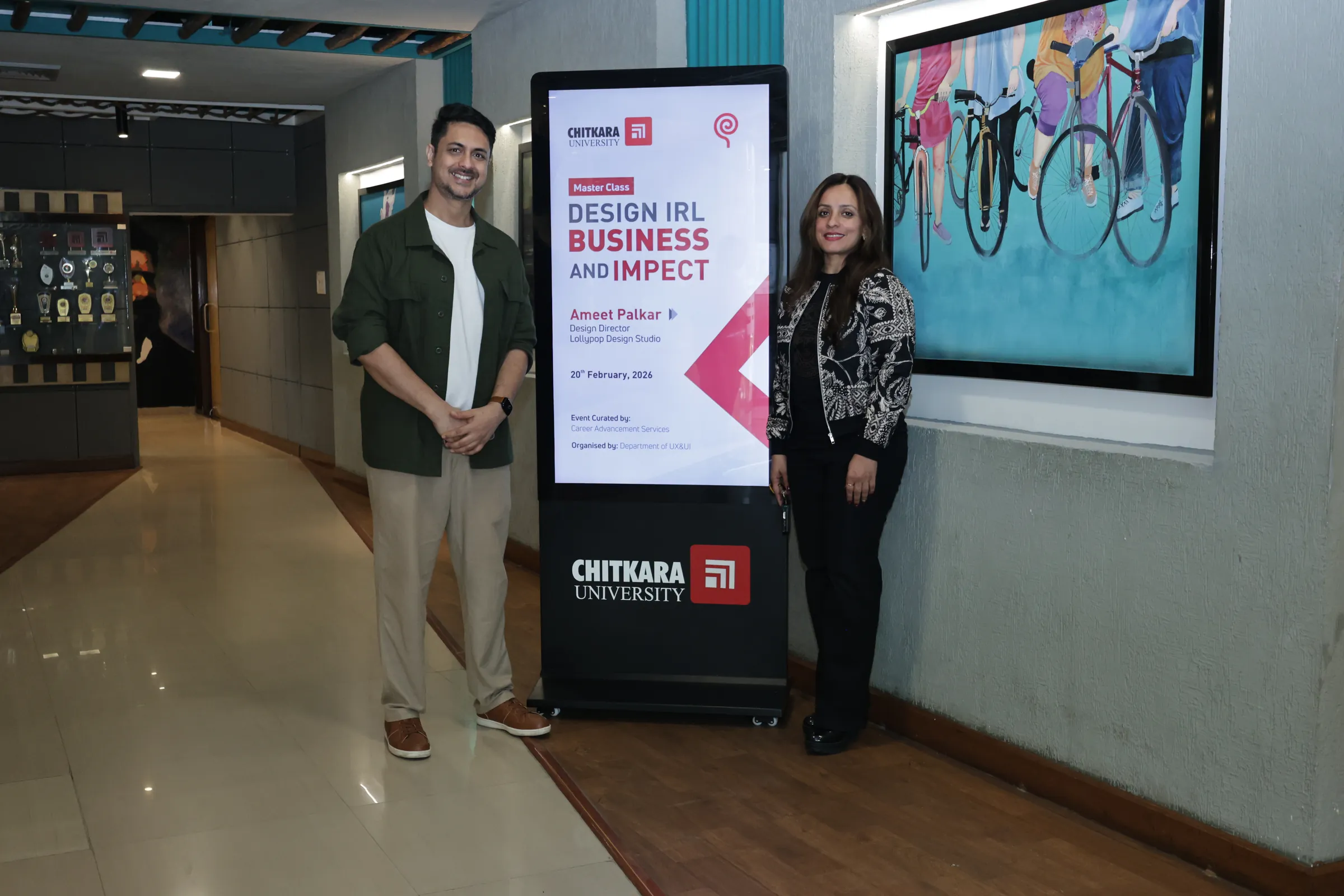 Ameet and another person standing either side of the event poster for the master class