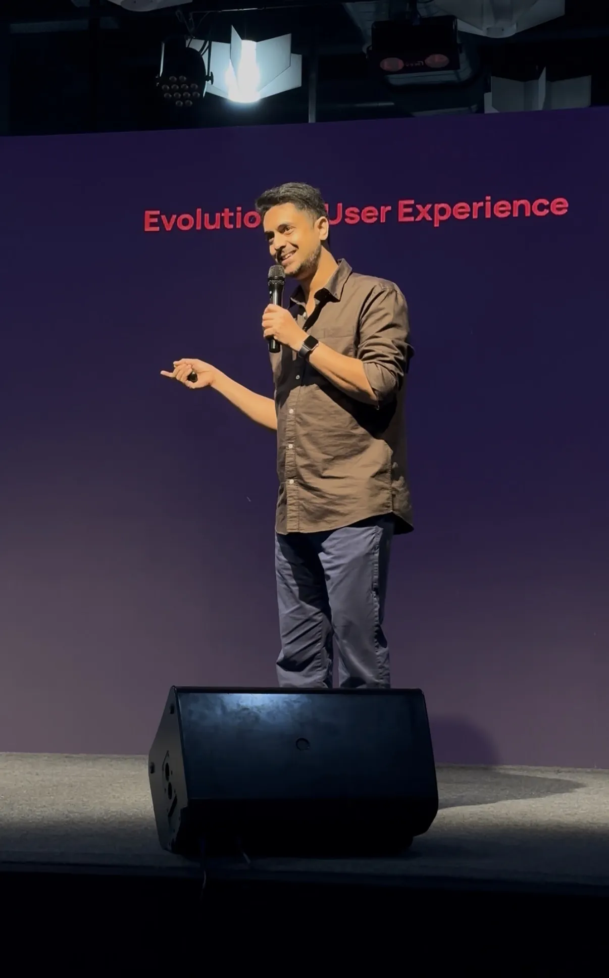 Ameet Palkar smiling on stage at Salesforce Design Days, microphone in hand, with the words Evolution of User Experience on the screen behind him